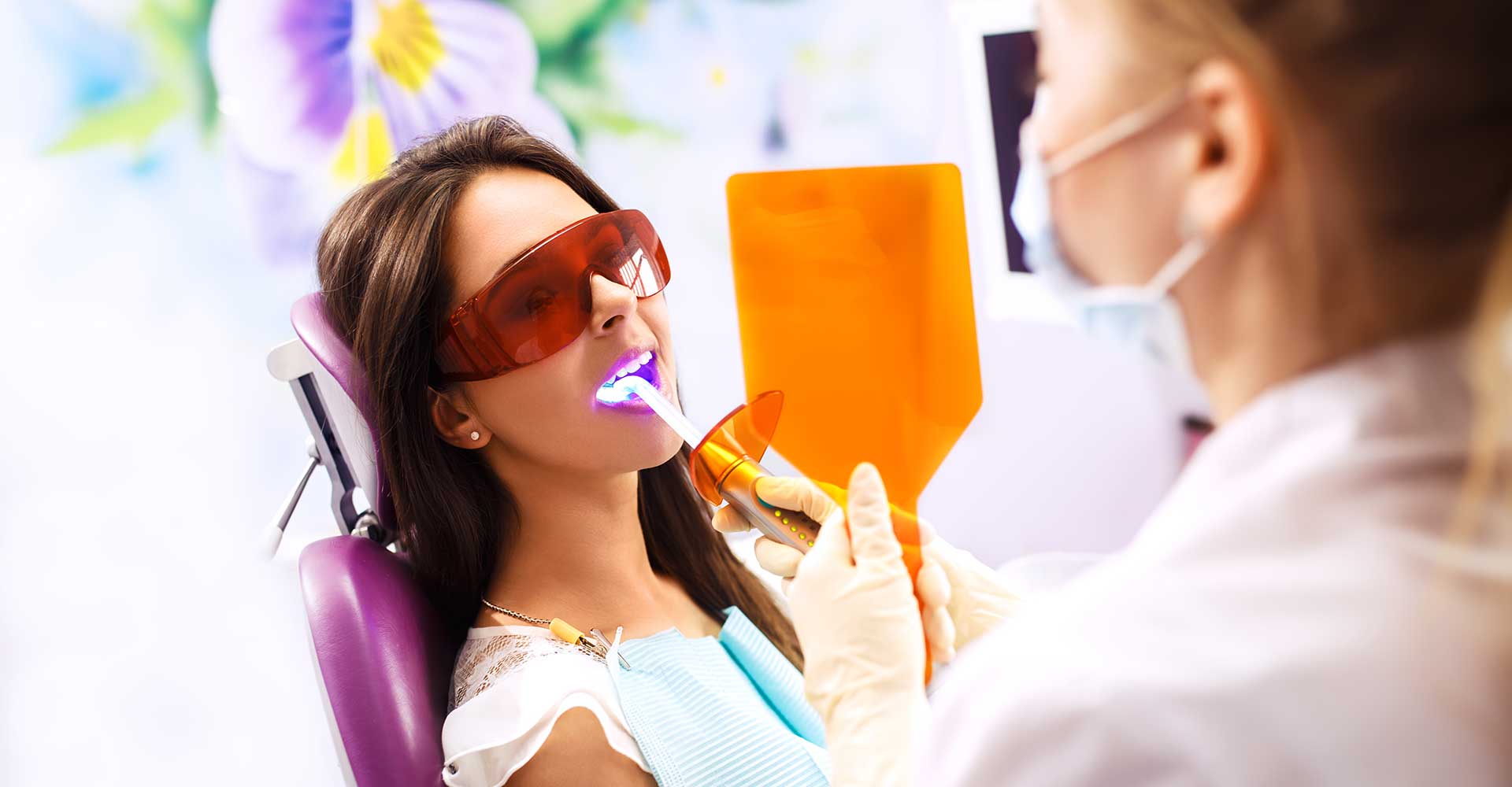 Dentist performs teeth whitening with UV light.