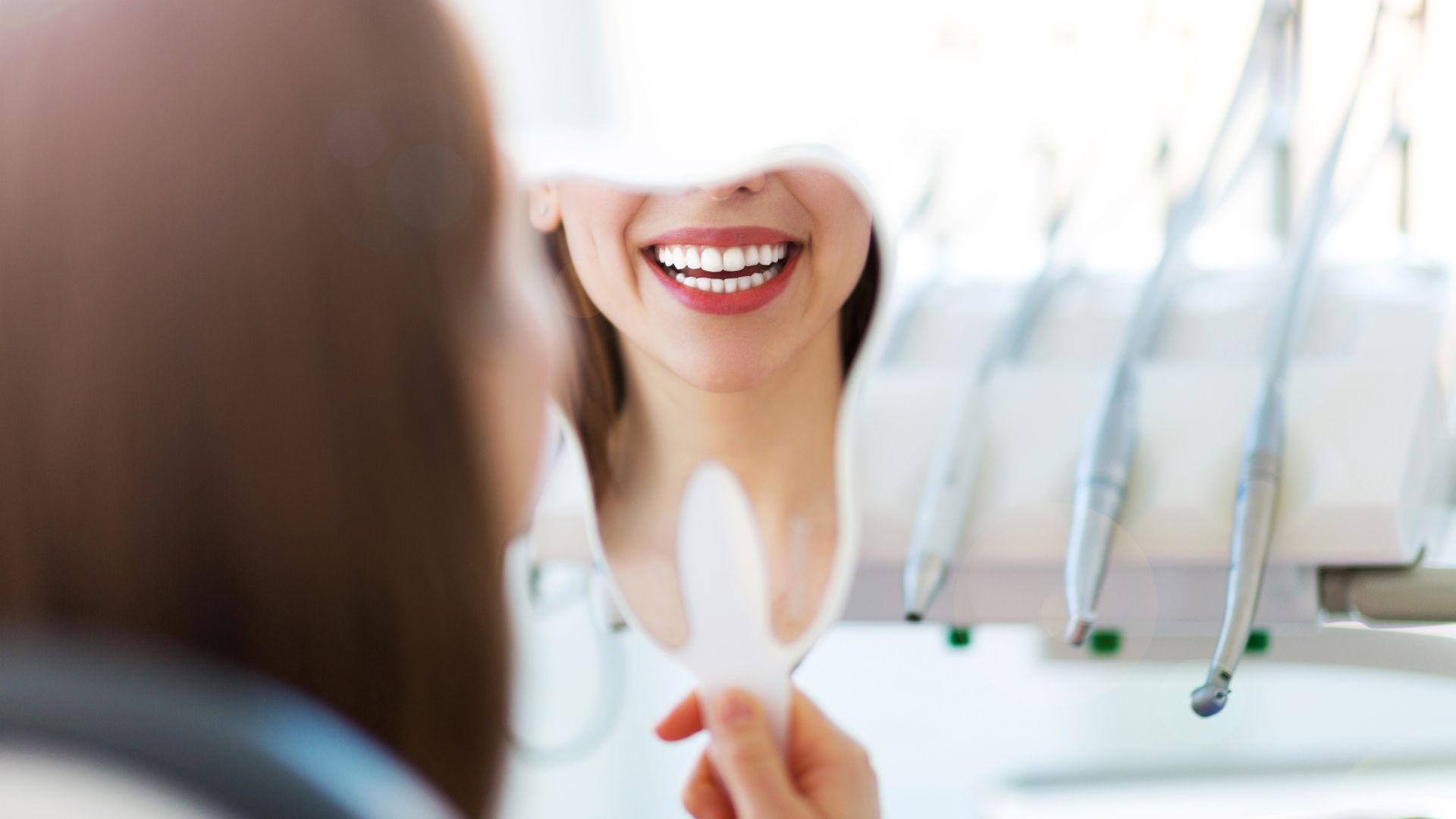 Woman smiling at teeth in dental mirror.