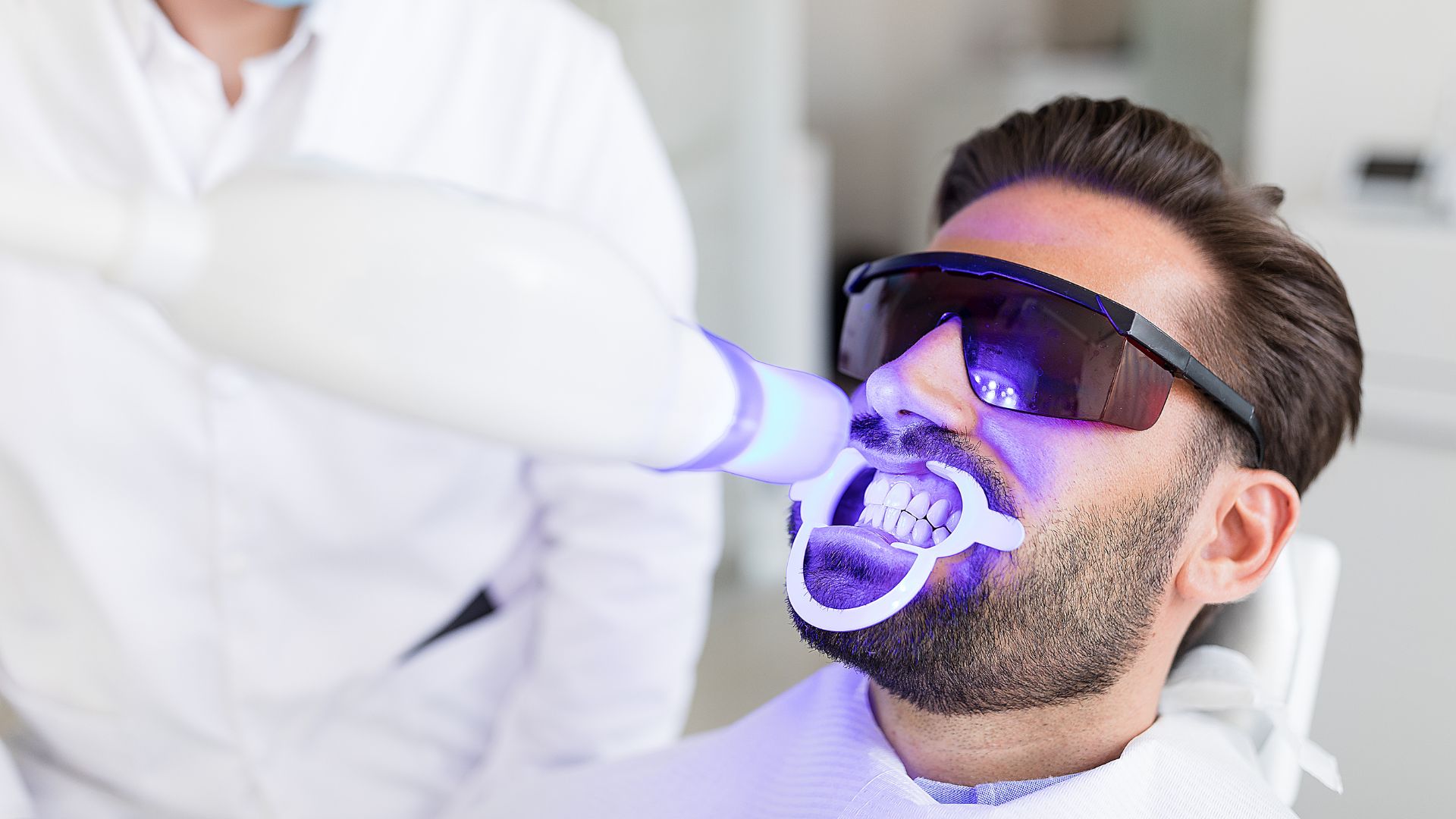 Man receiving teeth whitening treatment at dentist.