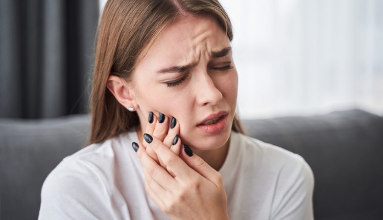 Woman experiencing toothache, holding her cheek.