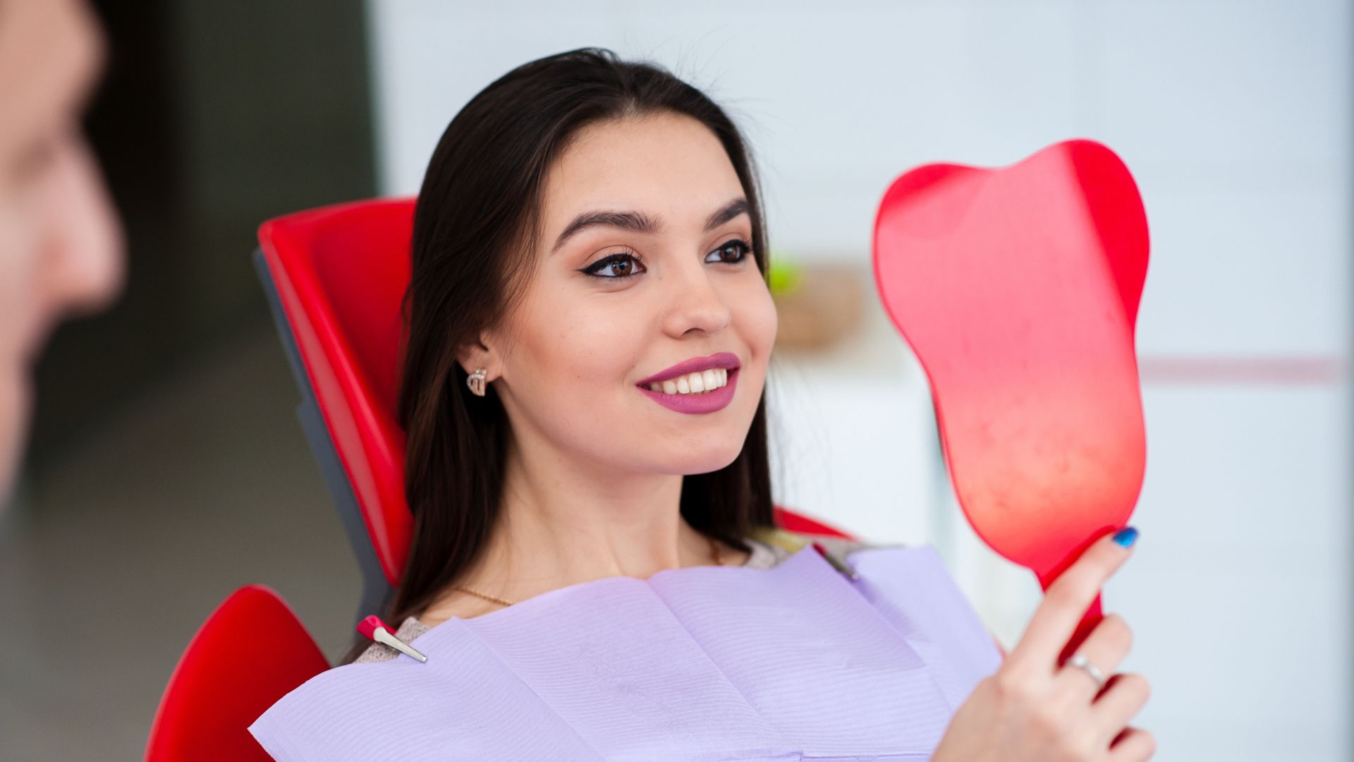 Woman smiling, holding a red dental mirror.